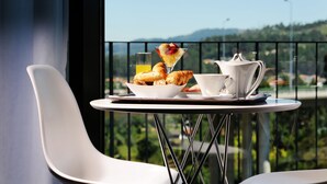 A breakfast setup on a balcony with croissants, a fruit drink, a fruit salad, and a coffee pot. - Open Village Sports Hotel & SPA Club (Guimarães)