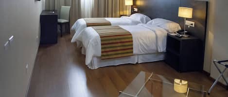 A hotel room with two beds, a desk, a chair, a lamp, and a glass table.