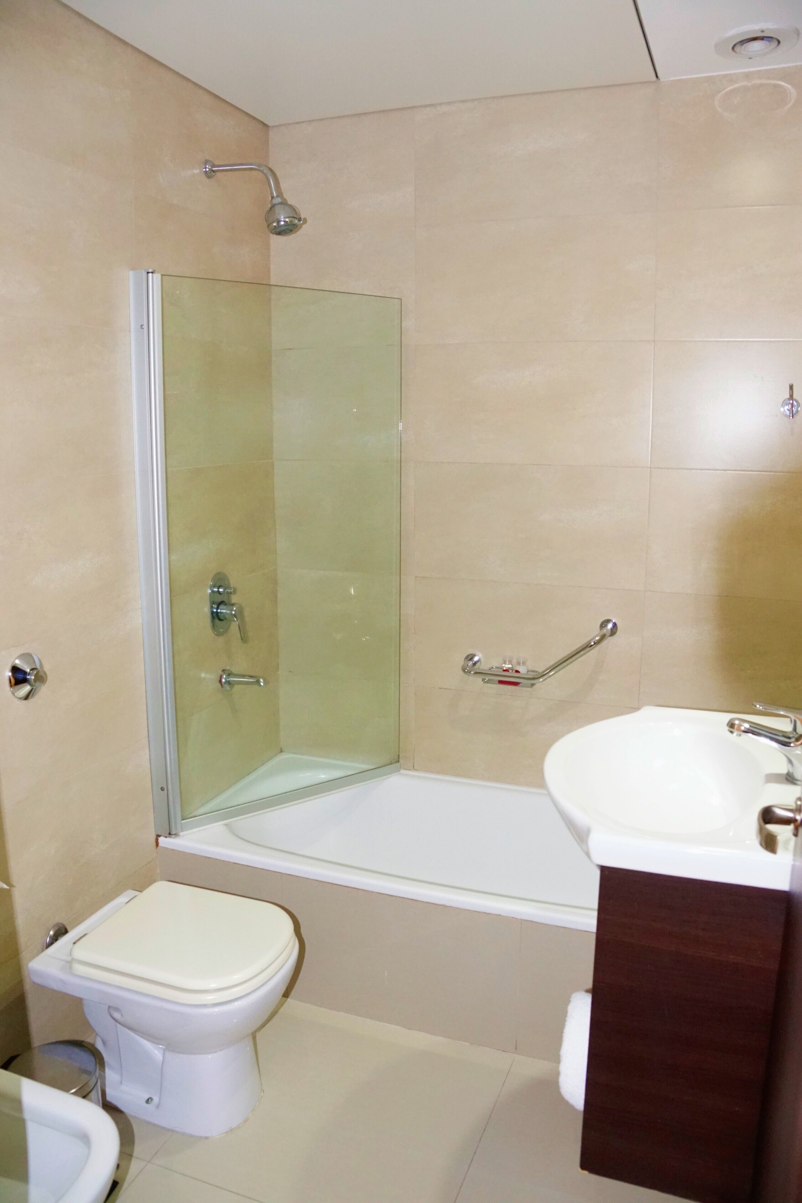 A bathroom with a glass-enclosed shower, a white toilet, and a sink with a wooden cabinet.