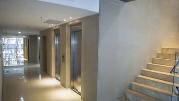 Un interior moderno con piso pulido, barandilla de vidrio en una escalera y pasillo que conduce a ascensores.