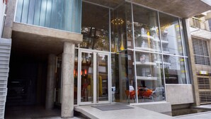 A modern building with large glass windows, a concrete facade, and a tiled entrance area.