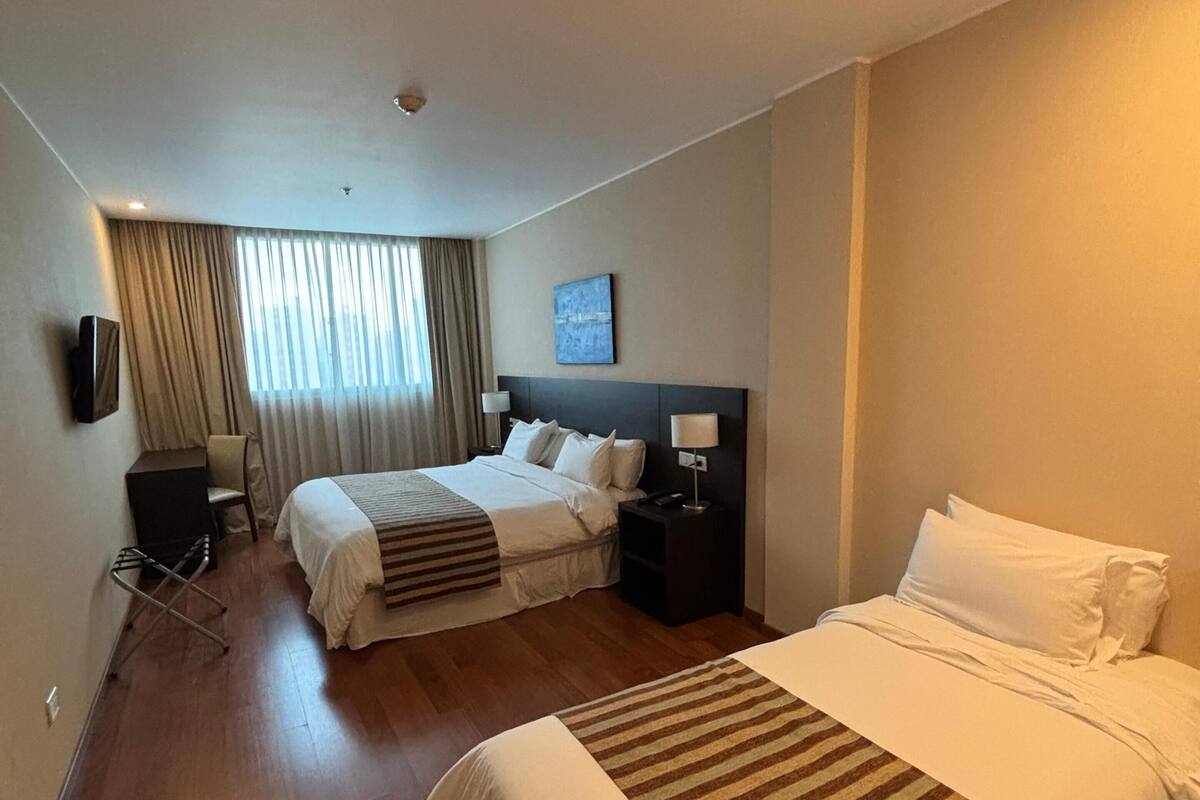 A hotel room with two beds, a TV, a desk, and a window with curtains.
