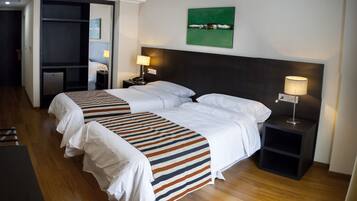 Quarto de hotel com duas camas, piso de madeira, pintura abstrata verde e mesa de cabeceira com abajur.