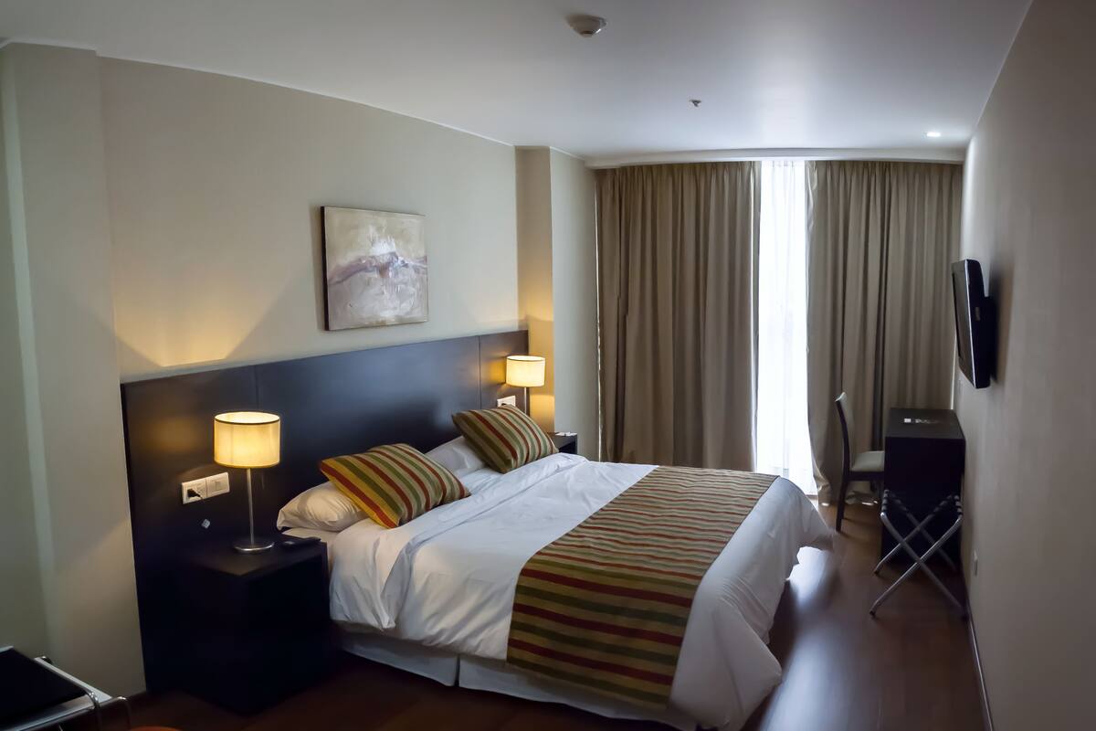 A hotel room with a large bed, two bedside lamps, a flat-screen TV, and a painting on the wall.