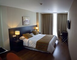 Habitación de hotel con una cama grande, dos lámparas de noche, un televisor de pantalla plana y un cuadro en la pared.