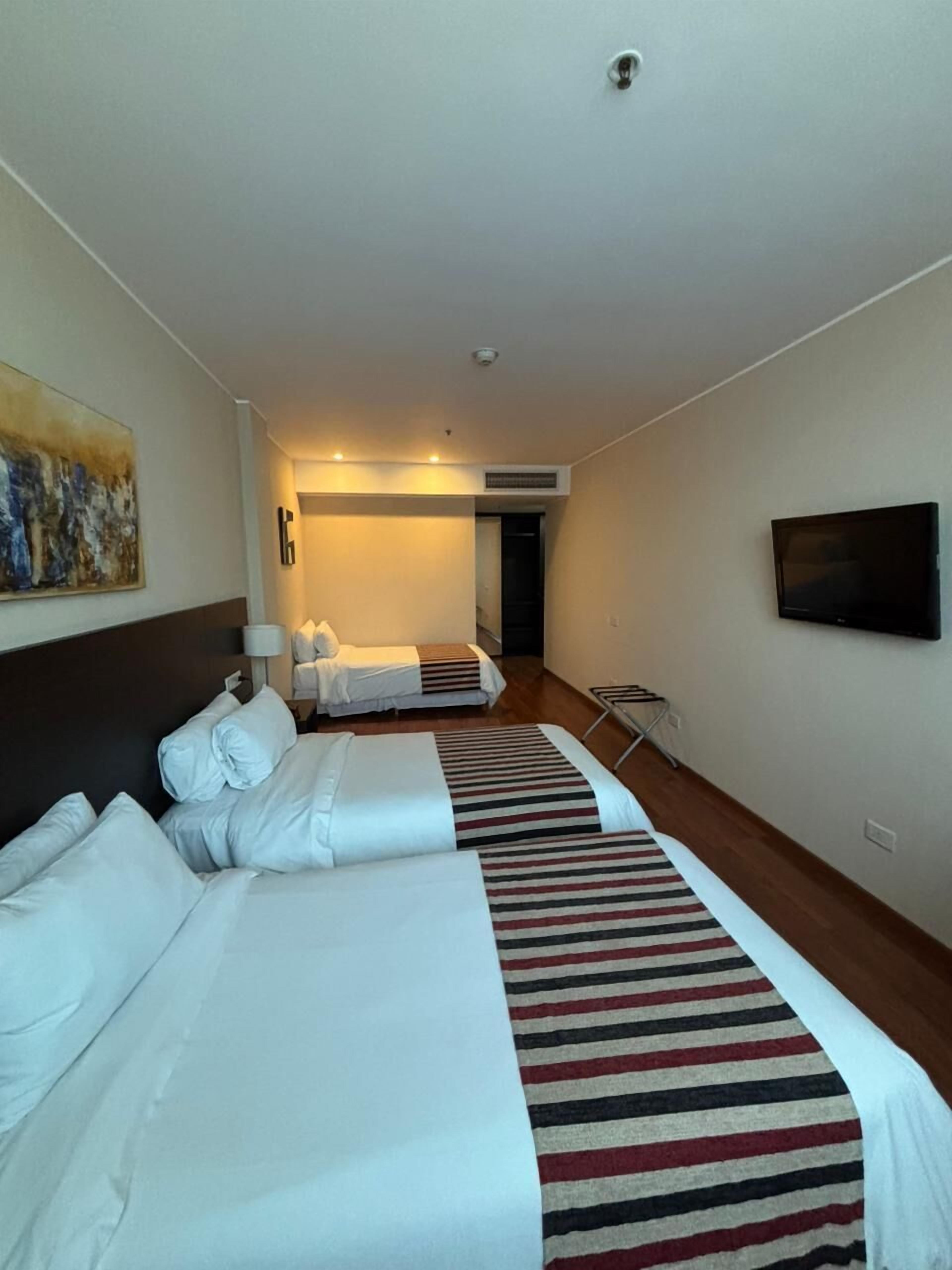 A hotel room with two beds, a TV, and a painting on the wall.