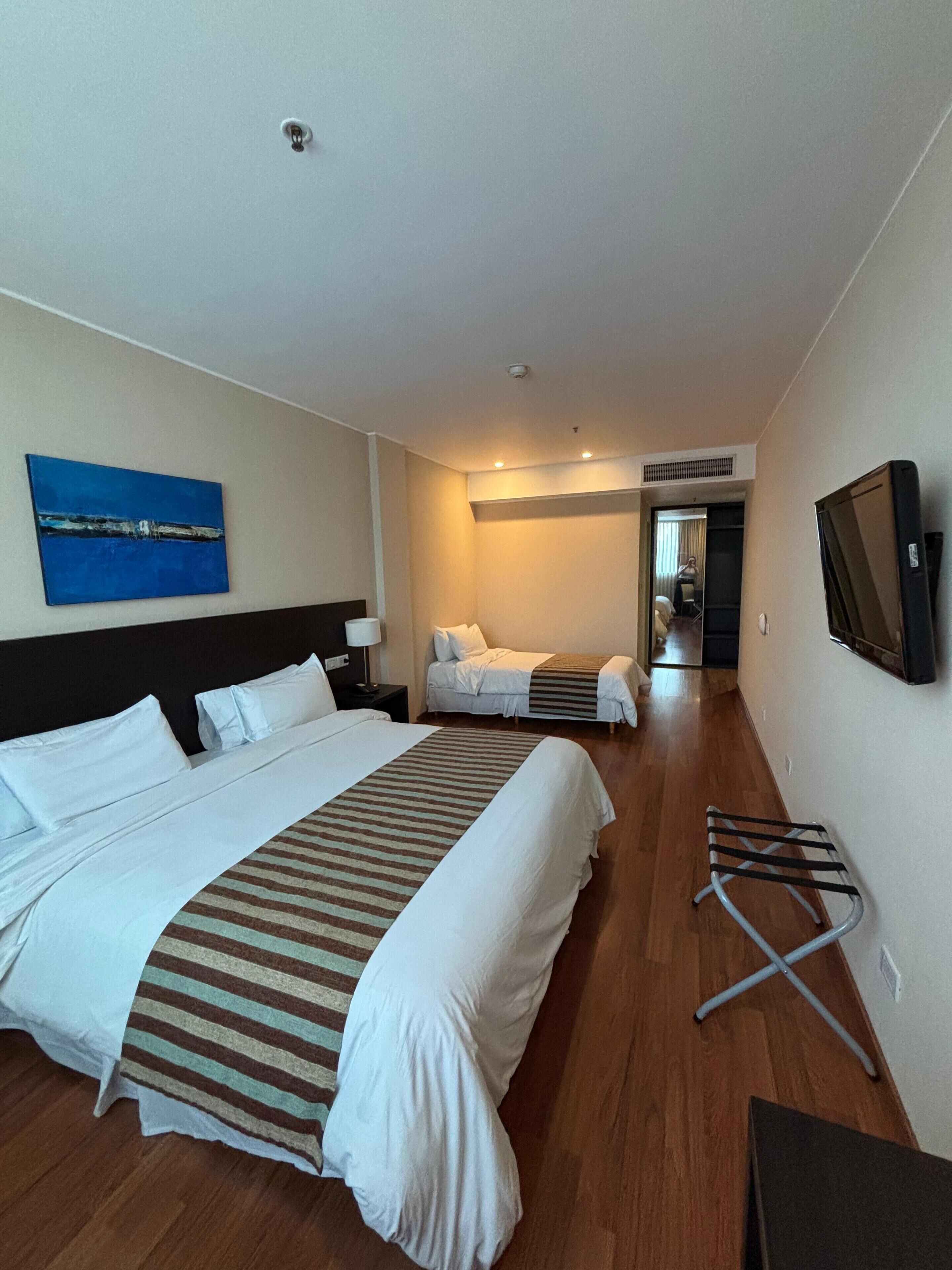 A hotel room with a large bed, a smaller bed, a TV, and a painting on the wall.