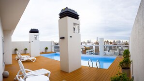 A rooftop pool area with lounge chairs, a pool, and a city view.