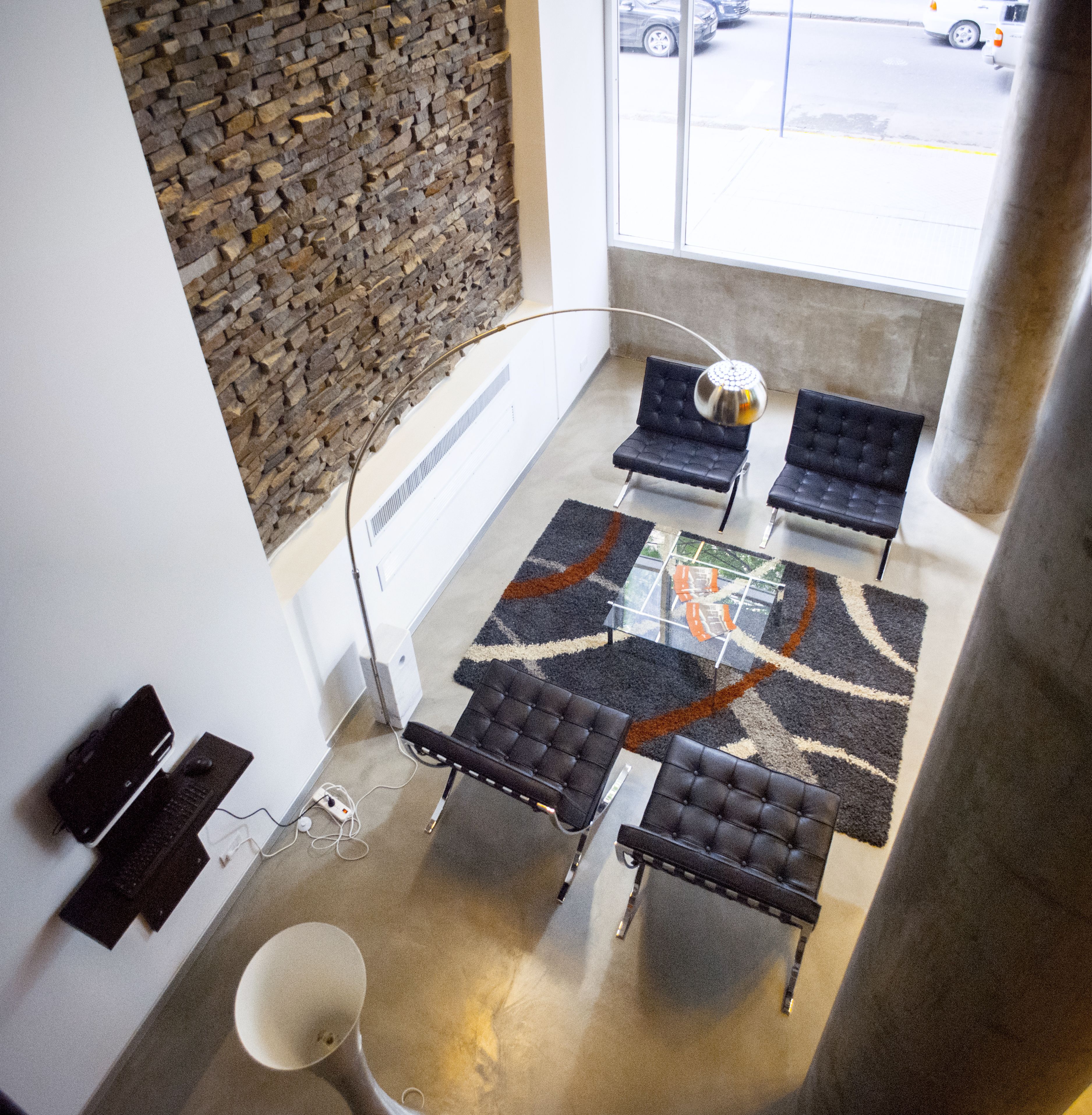 Un intérieur moderne avec un mur en pierre, une table en verre et des fauteuils en cuir noir.
