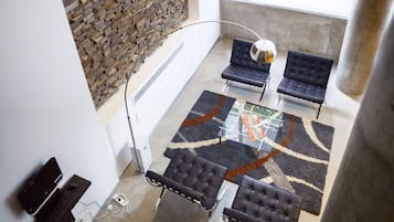 A modern interior with a stone wall, a glass table, and black leather chairs.
