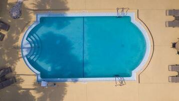 Vista aérea de una piscina rectangular con borde de azulejos, rodeada de sillas de descanso y sombrillas.