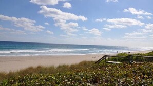 A beach with waves, a clear sky, and a wooden walkway. - Getaways At Dover House (Delray Beach)
