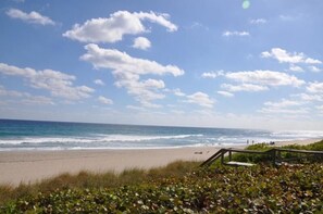 Una spiaggia con onde, cielo sereno e una passerella di legno.
