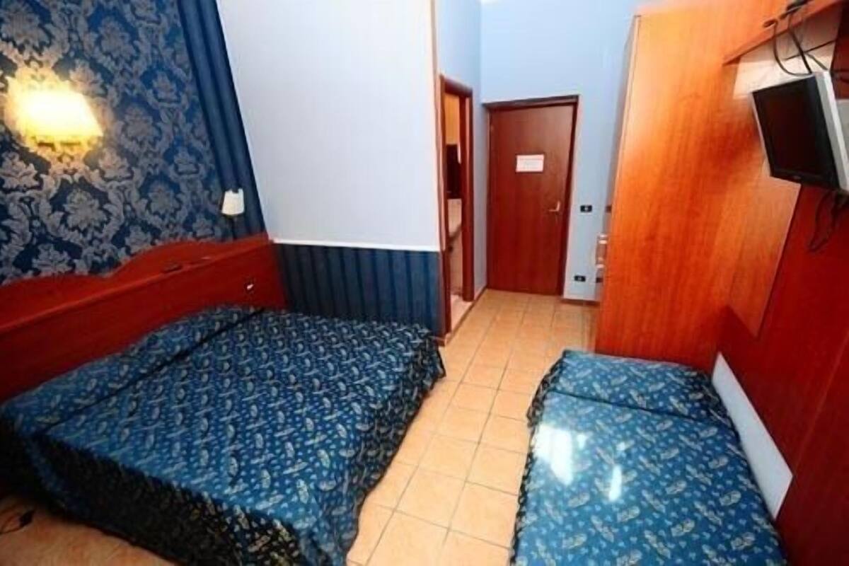 A small room with two beds, a wooden wardrobe, a television, and a door leading to another room.