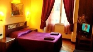 Quarto de hotel com cama, escrivaninha, cadeira, televisão e janela com cortinas.