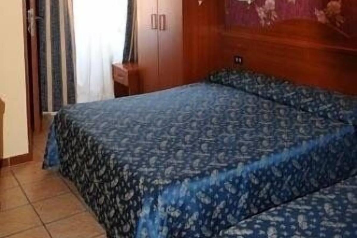 A hotel room with a bed, a wardrobe, a desk, and a ceiling fan.