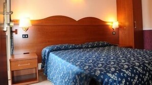 Quarto com cabeceira de madeira, duas luminárias de cabeceira, mesa de cabeceira de madeira e colcha estampada.