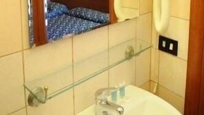 Casa de banho com espelho, lavatório, prateleira de vidro, secador de cabelo e chuveiro.
