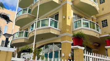 Un hotel de varios pisos con balcones, un cartel que da la bienvenida a los huéspedes al Baker's Suites Boutique Hotel y una cerca blanca de piquetes.