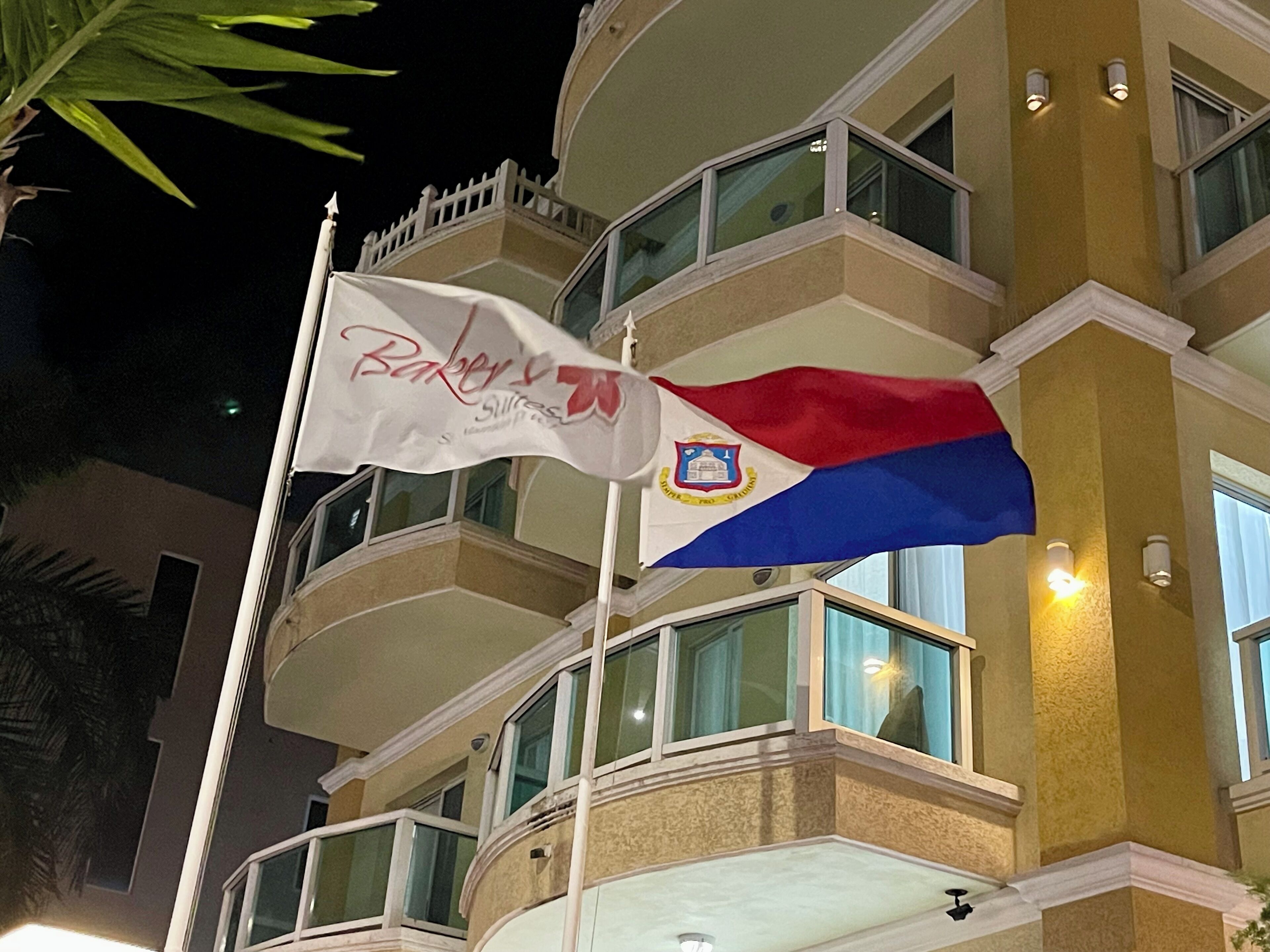 En hotelbygning med flere balkoner, et flag med et logo, og aftenbelysning.