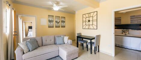 A living room with a sectional sofa, a dining table with chairs, and a ceiling fan.