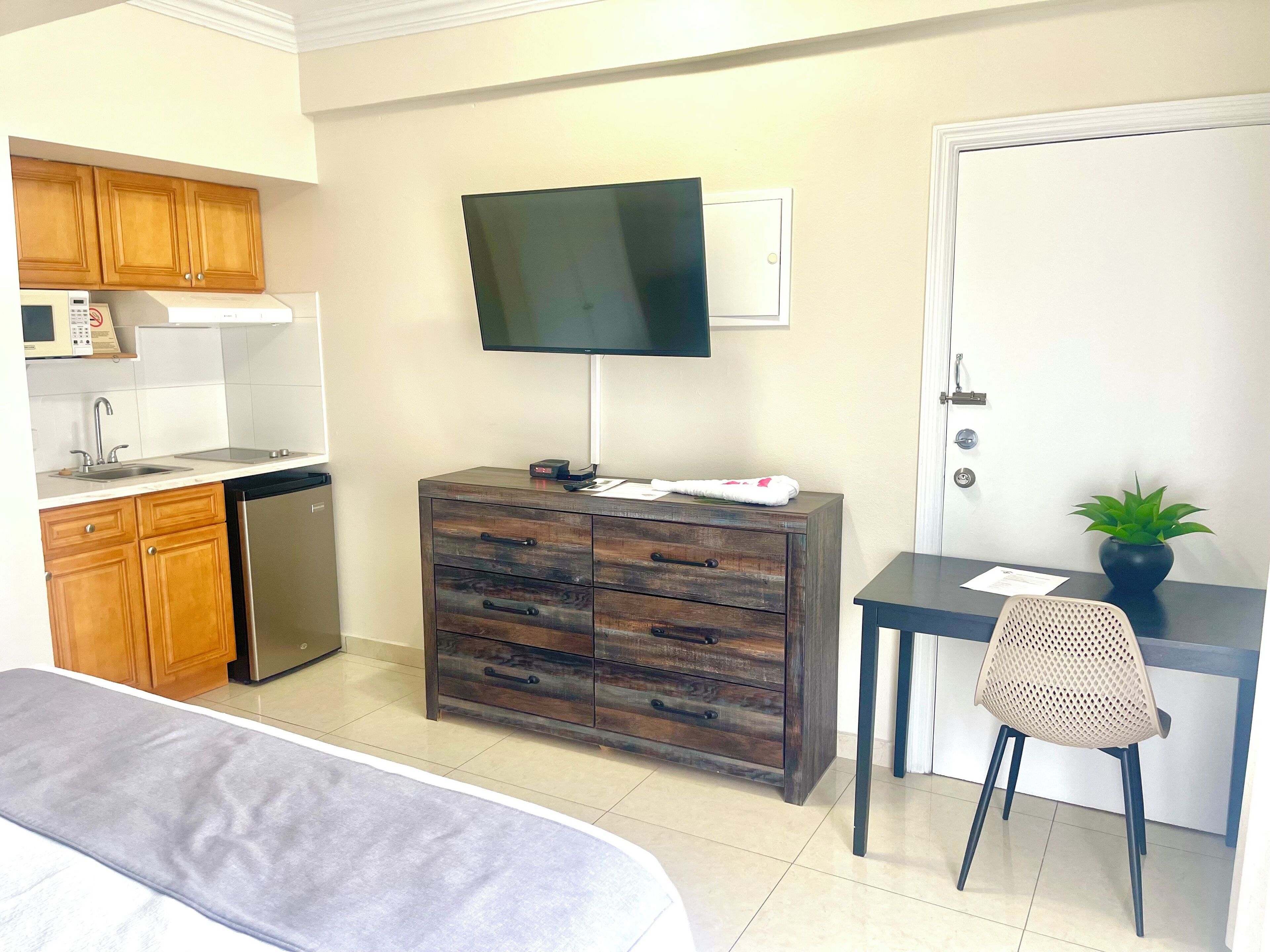 Habitación compacta con kitchenette, cama, escritorio con silla y televisión montada en la pared.