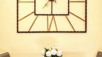 Un reloj de pared con diseño geométrico, una mesa con dos sillas y un jarrón con flores blancas.