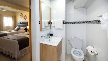 A hotel bathroom with a white sink, a toilet, and a shower area. There is a mirror above the sink and a towel rack on the wall.