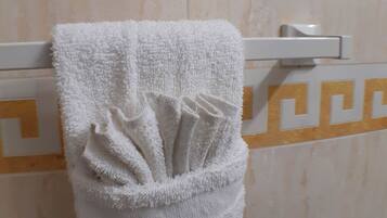 Un asciugamano bianco appeso a un portascopevoli bianco in un bagno con parete in marmo e motivo geometrico.