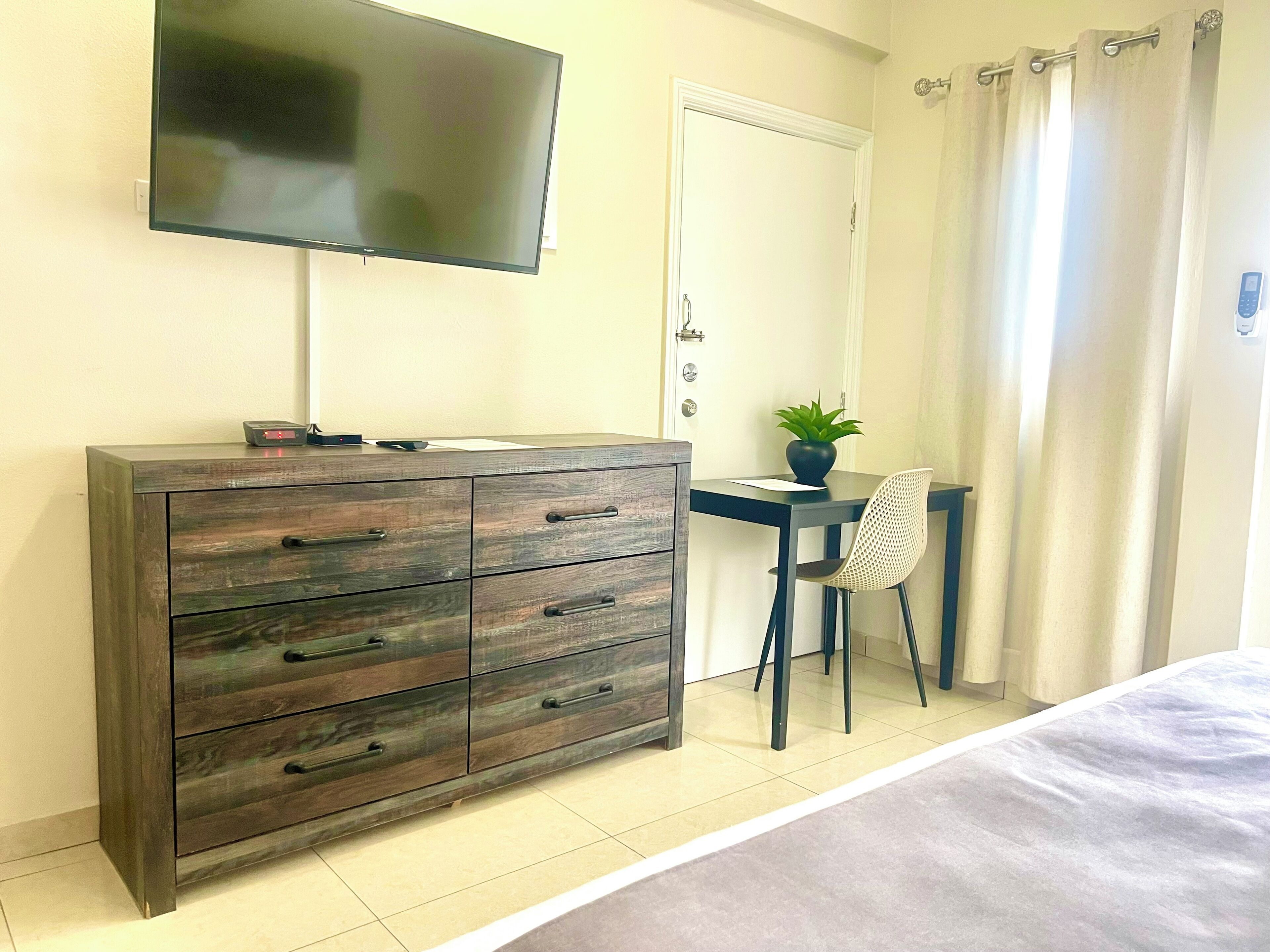 Un dormitorio con cama, cómoda, escritorio con silla, televisor y puerta.