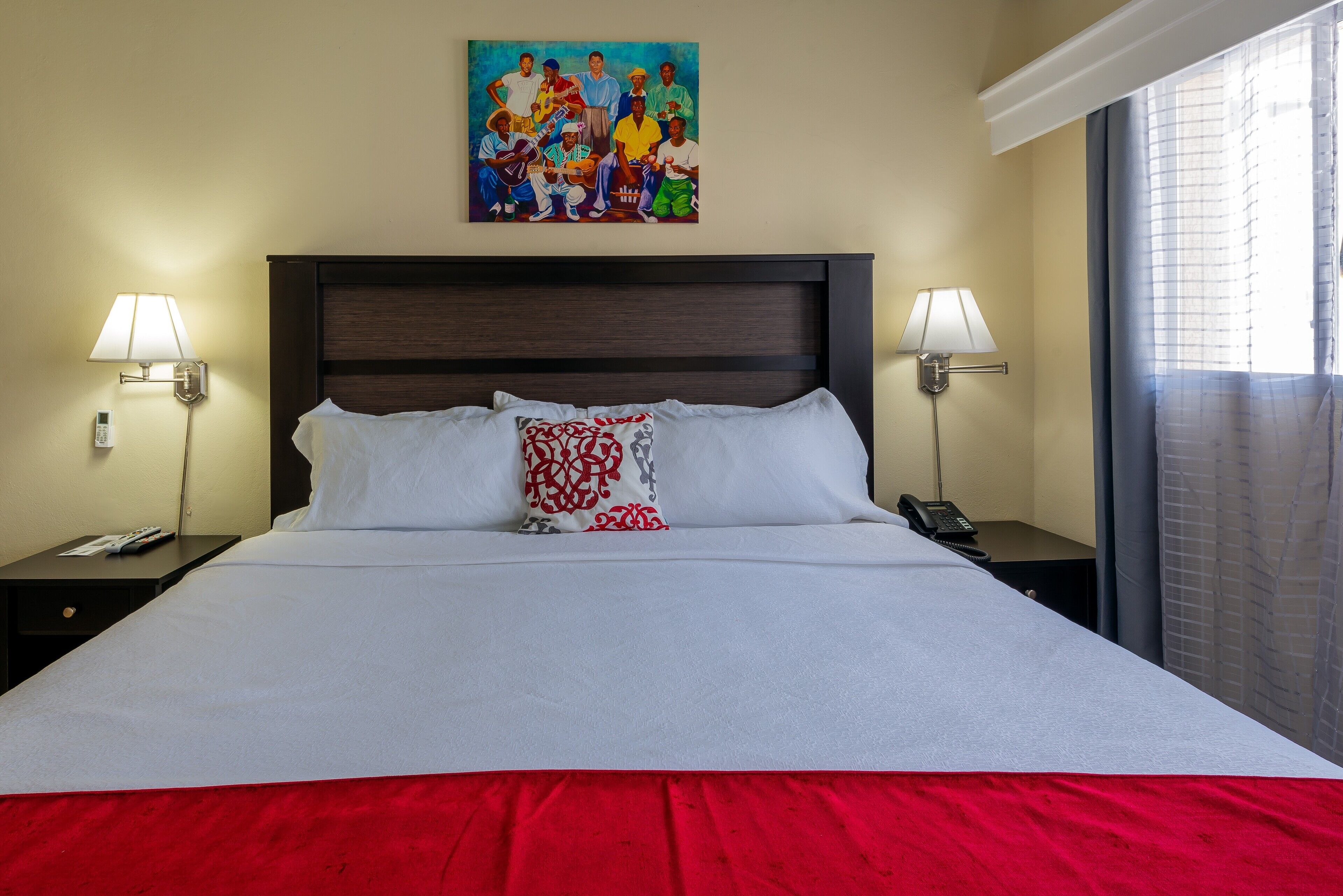 Una habitación de hotel con una cama grande, dos mesitas de noche, un cuadro sobre la cama y una ventana con cortinas.