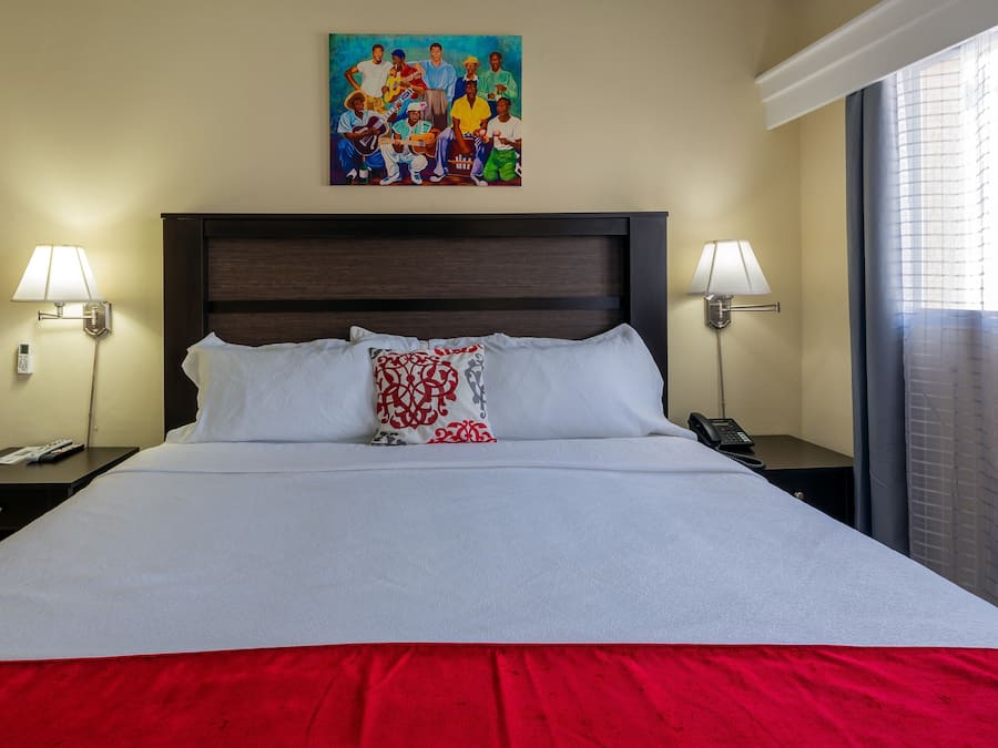 Una habitación de hotel con una cama grande, dos mesitas de noche, un cuadro sobre la cama y una ventana con cortinas.