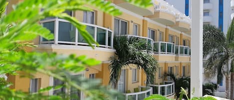Un hotel de varios pisos con balcones, una palmera y un cielo despejado.