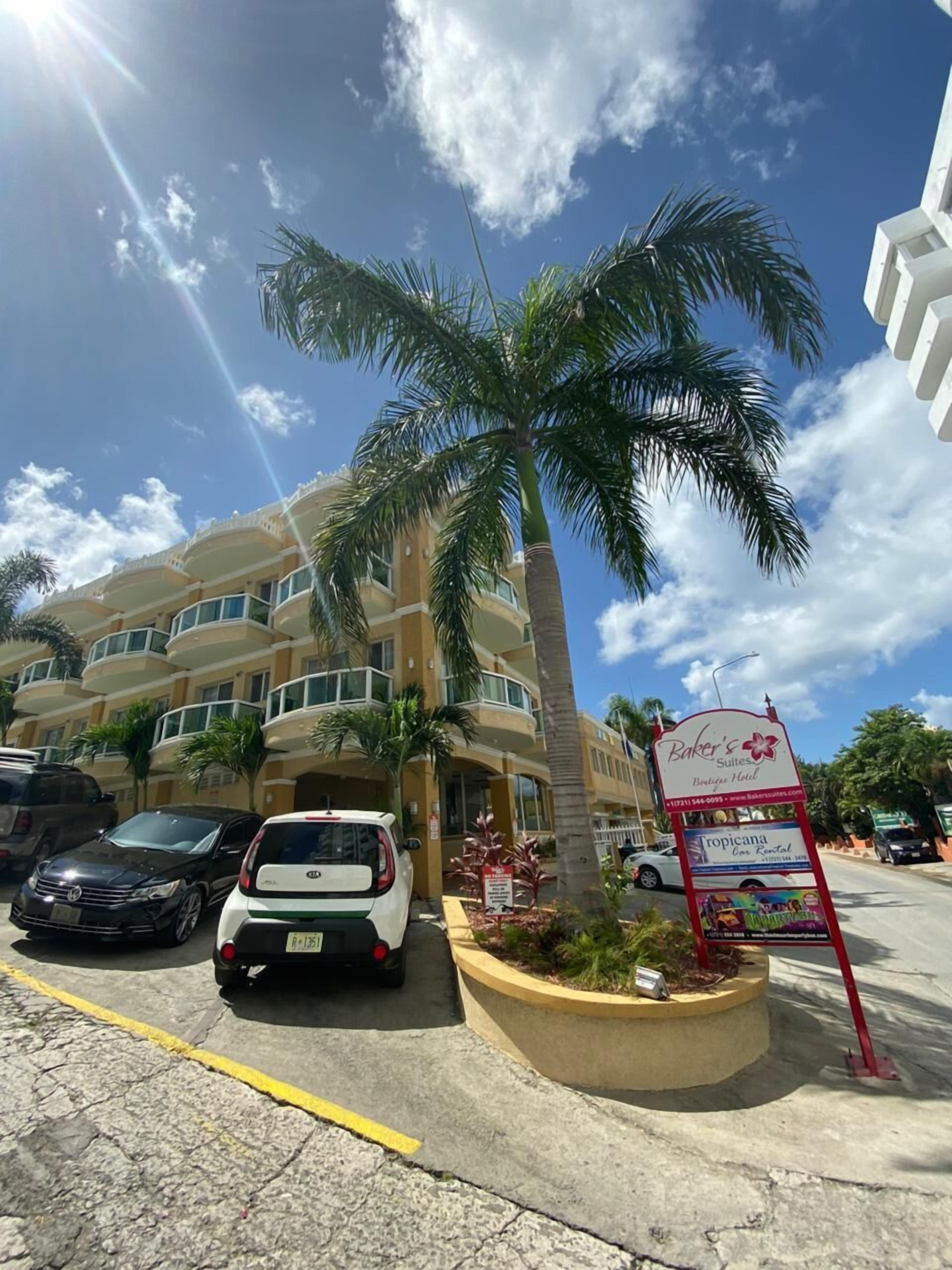 A hotel with a signboard, parked cars, and a palm tree.