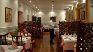 A restaurant with tables set for dining, a waiter attending to guests, and decorative panels along the walls. - Albert Premier (Algiers)
