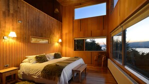 A bedroom with a large bed, wooden walls, a view of the outdoors, and a window with a view of the landscape. - OCIO Territorial Hotel (Castro)