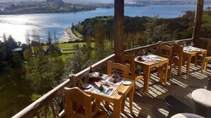 A wooden deck with tables and chairs overlooking a lake and beach. - OCIO Territorial Hotel (Castro)