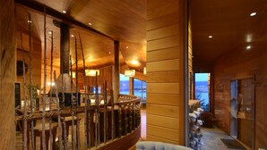 A wooden interior with a dining area featuring a rustic wooden railing, a tufted chair, and a view through large windows. - OCIO Territorial Hotel (Castro)