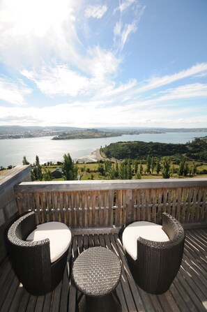 A wooden deck with wicker furniture overlooking a lake and distant cityscape.
