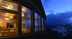 A modern building with large windows overlooking a body of water and a cityscape at night.