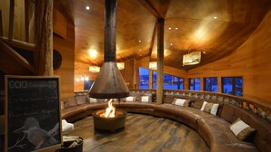 A cozy, wood-paneled lounge with a central fire feature, comfortable seating, and large windows offering a view of the cityscape. - OCIO Territorial Hotel (Castro)