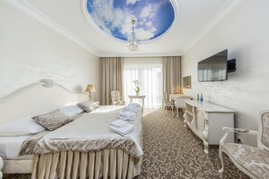 A hotel room with a large bed, a desk, a chair, a television, and a ceiling with a cloud design. - Hotel Kiston (Suleczyno)