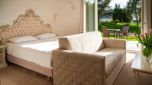 A bedroom with a large bed, a sofa, and a table with a vase of flowers. - Hotel Kiston (Suleczyno)
