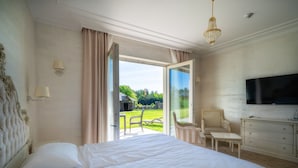 A bedroom with a large bed, a TV mounted on the wall, a chair, a small table, and a view of the outdoors. - Hotel Kiston (Suleczyno)