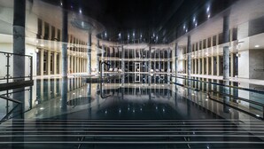 A spacious indoor swimming pool with clear glass walls, a central water feature, and a modern architectural design. - Hotel Kiston (Suleczyno)
