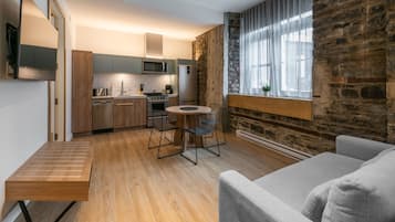 A modern kitchen with wooden cabinets, a dining area with a round table and chairs, and a stone wall with a window.