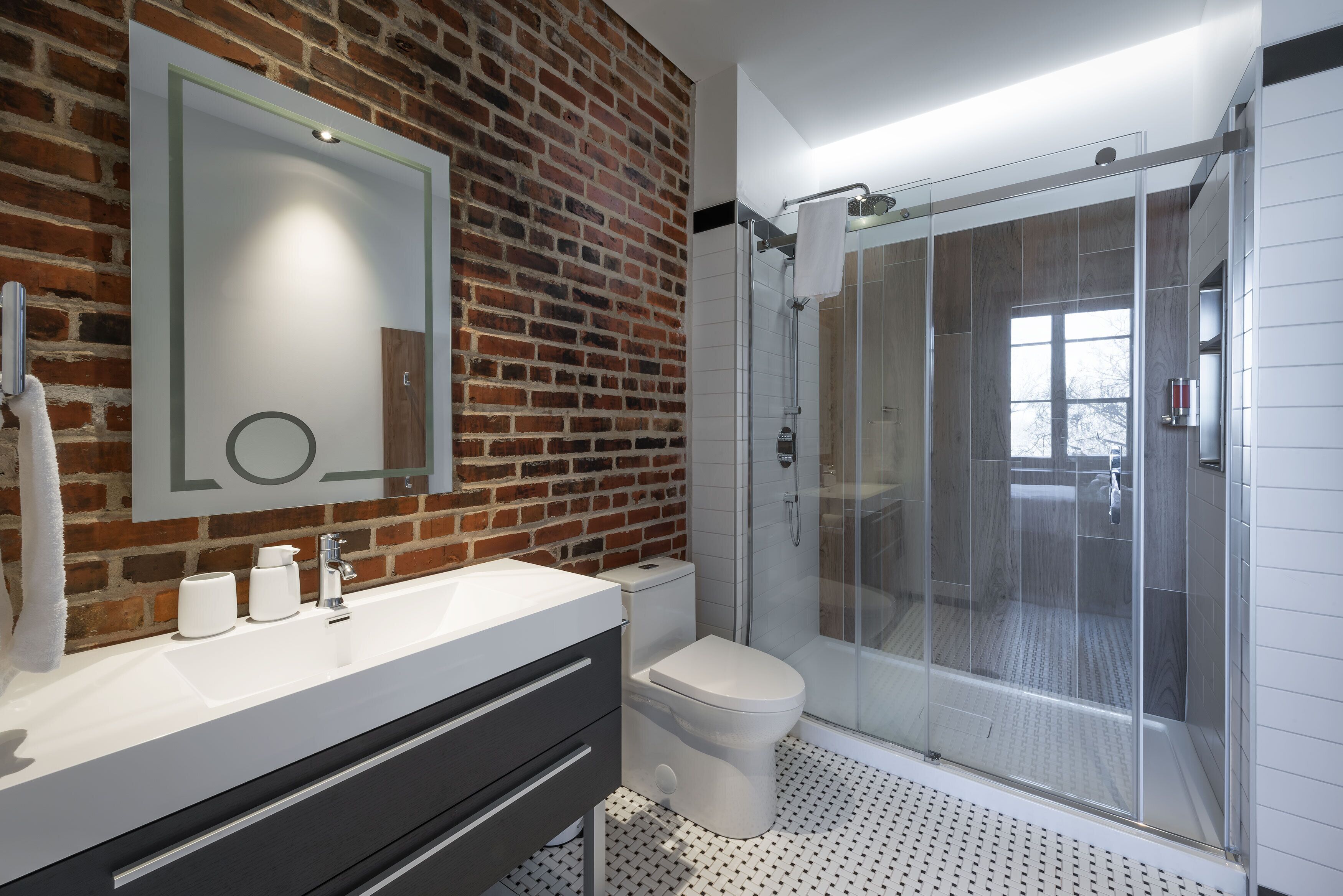 Een moderne badkamer met een bakstenen muur, een glazen douchecabine en een wit wastafelmeubel met spiegel.