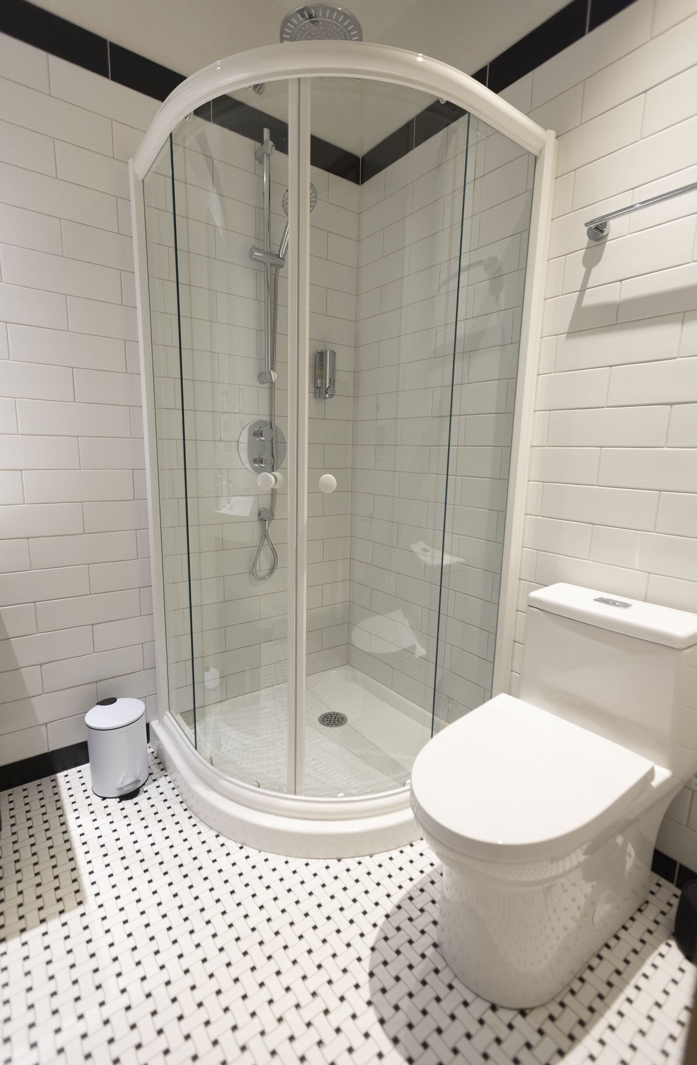 A modern bathroom with a glass-enclosed shower, white tiled walls, a white toilet, and a patterned floor.