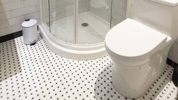 A modern bathroom with a glass-enclosed shower, white tiled walls, a white toilet, and a patterned floor.