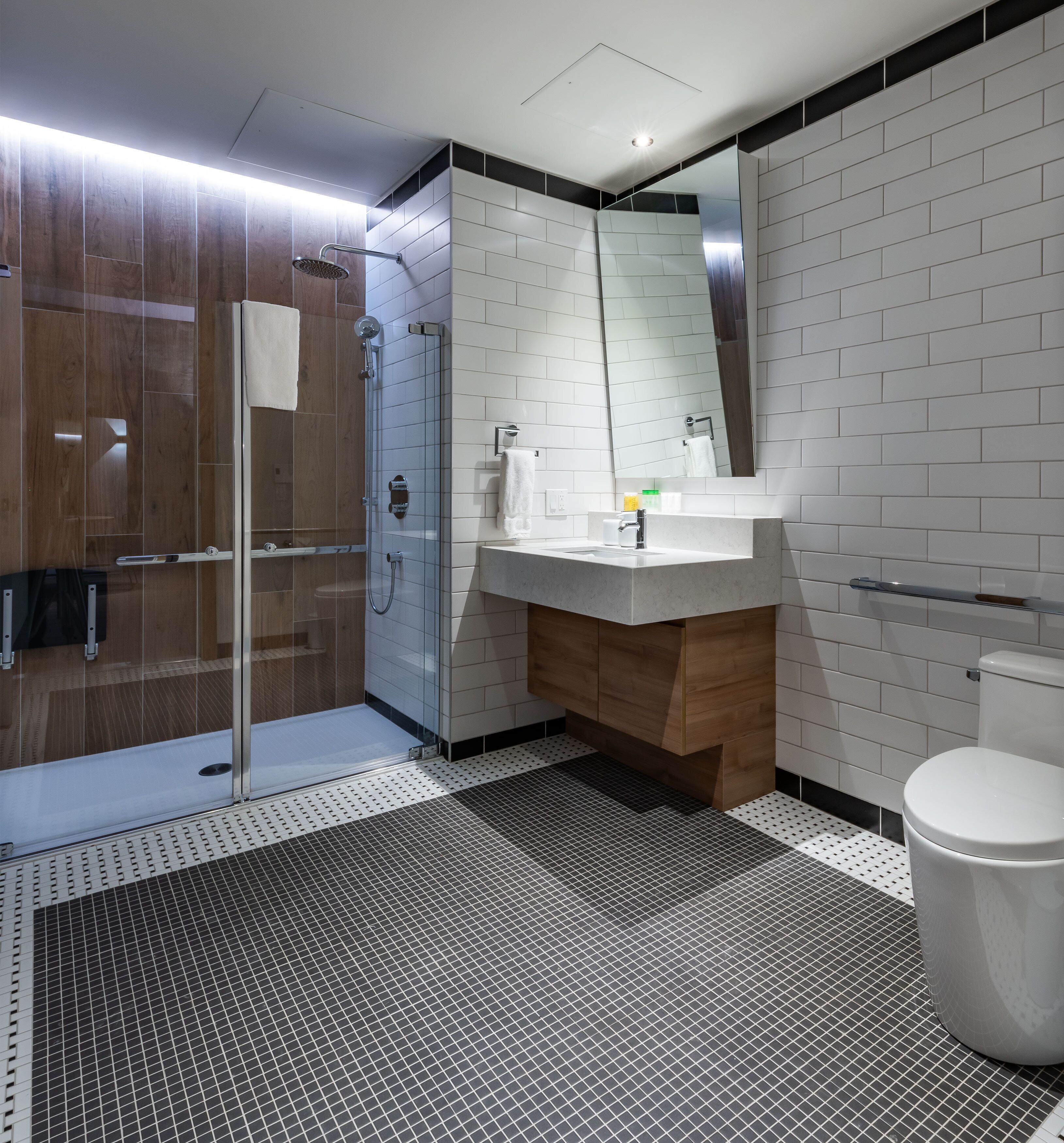 A modern bathroom with a glass shower enclosure, a white sink with a mirror above it, and a toilet.